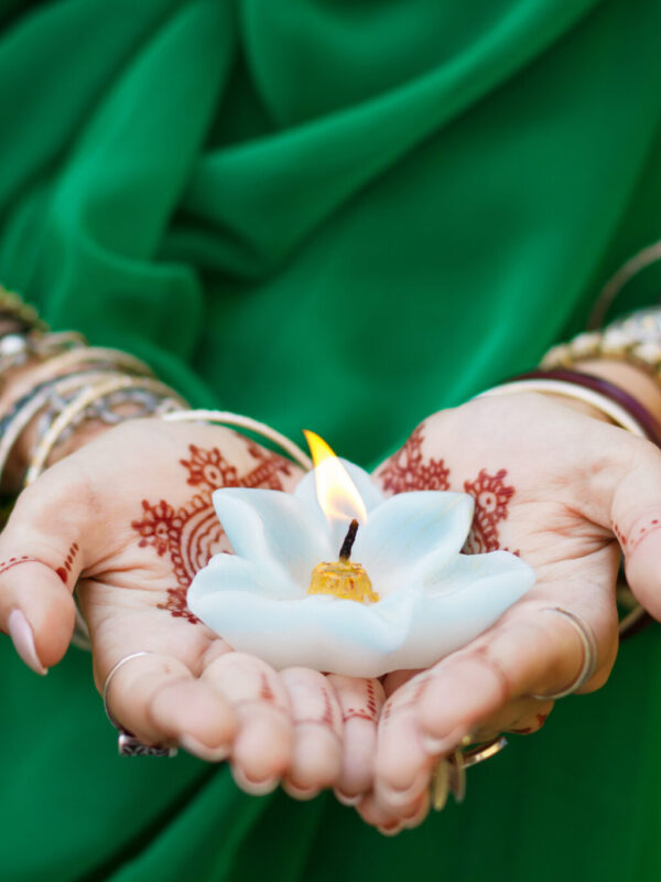 Beautiful woman in traditional Muslim Indian wedding green sari dress hands with henna tattoo mehndi pattern jewelry and bracelets hold burning lotus candle Summer culture festival celebration concept